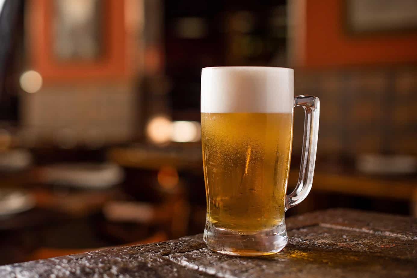 Frontier-style homemade beer in a glass mug on a rustic wooden table.