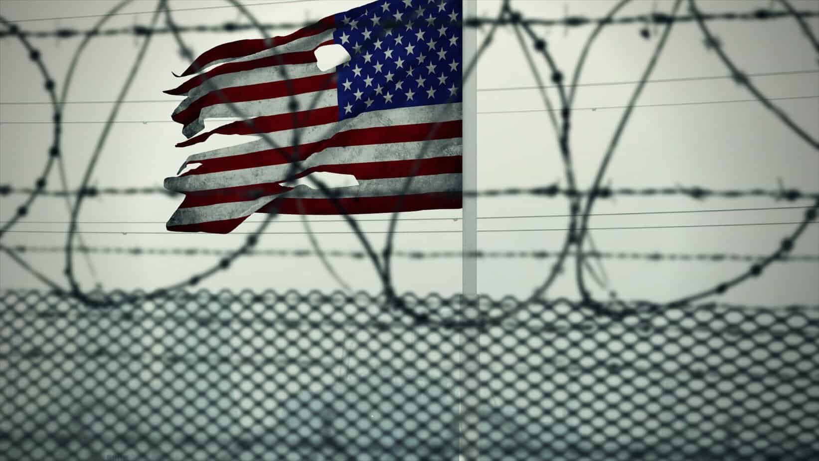 Torn American flag seen through razor wire, symbolizing restricted rights when prepping with a criminal record