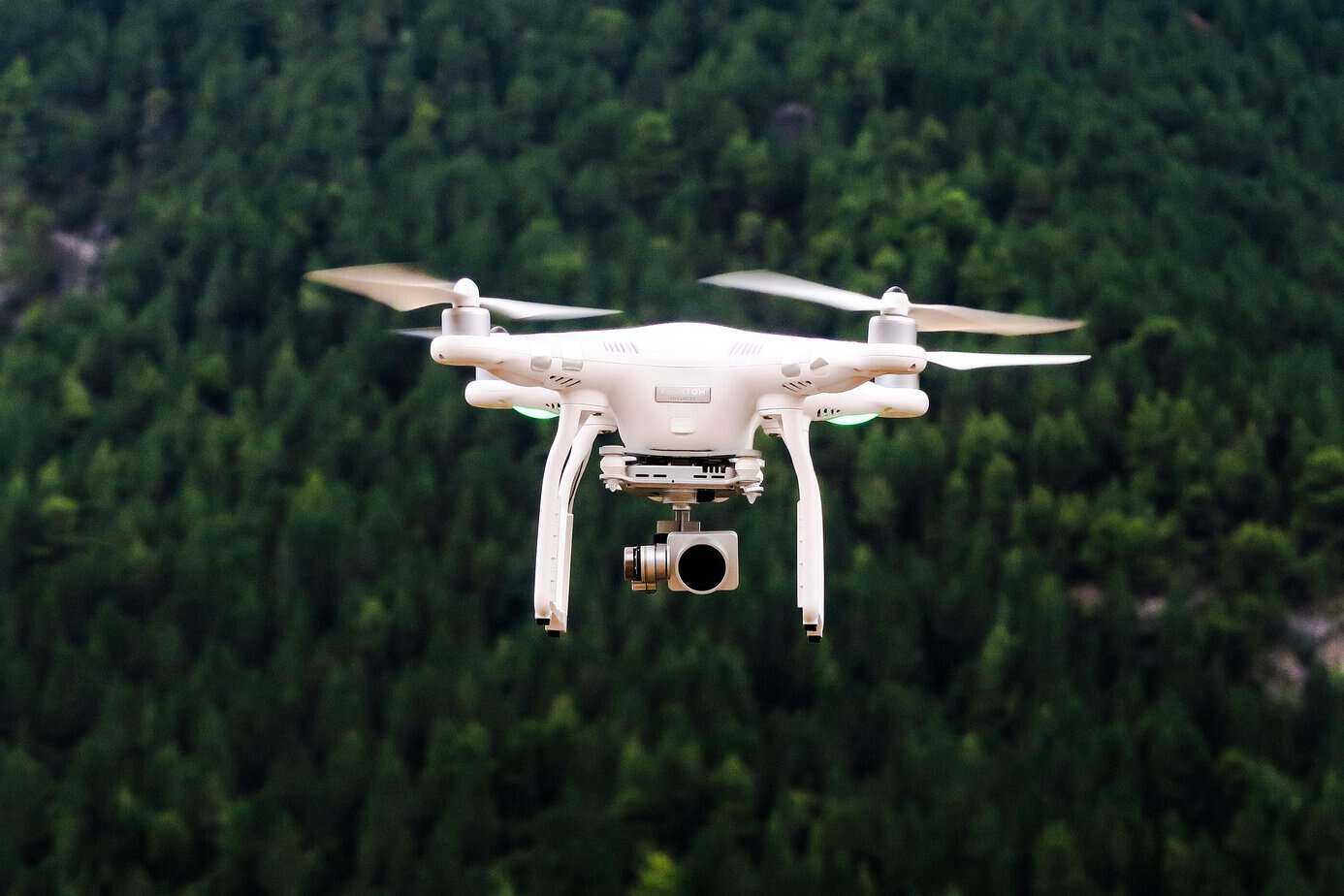 White quadcopter drone with gimbal camera hovering over dense forest, showing why off-grid land is not untraceable