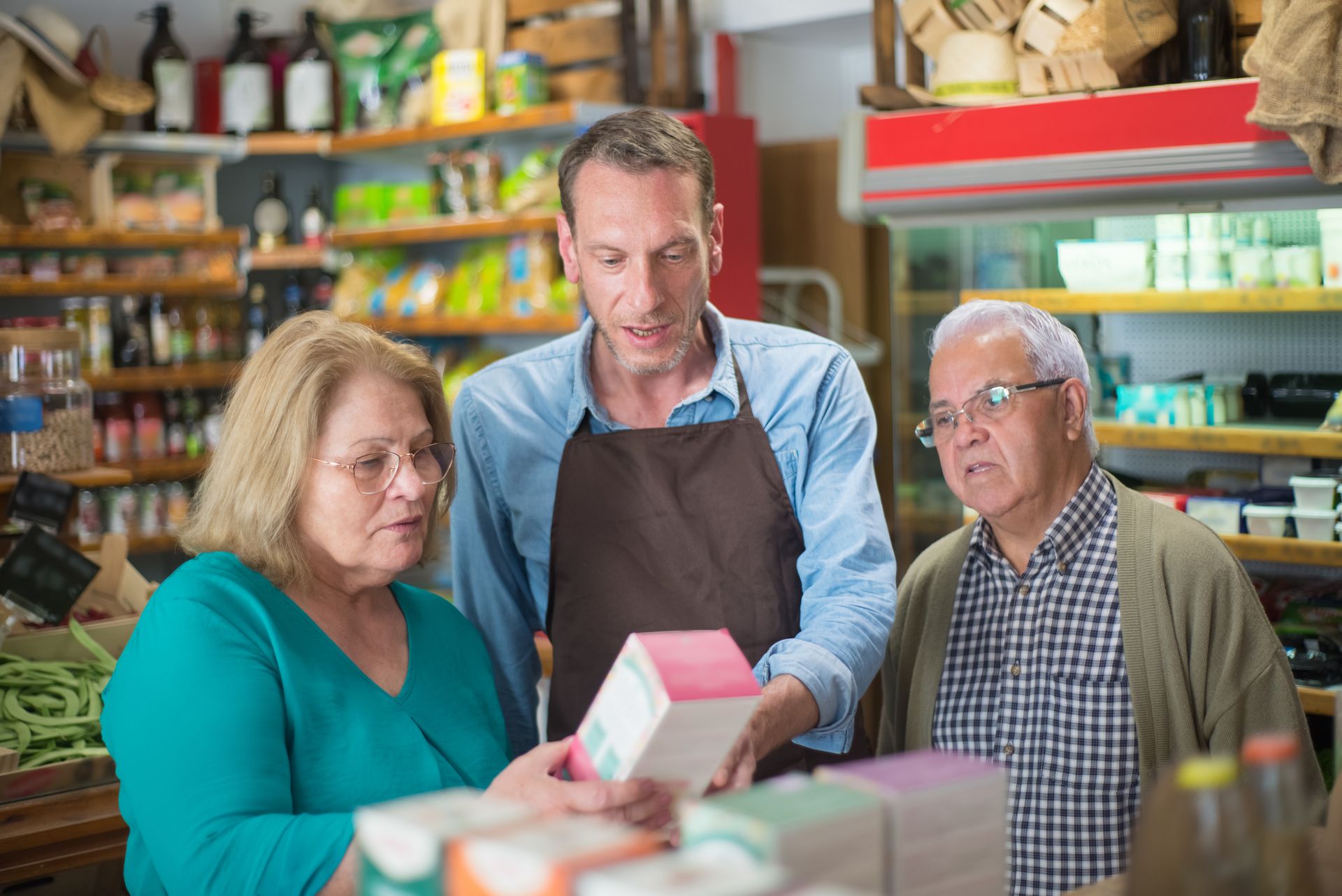 Older couple checking a product price with a grocery clerk as inflation in 2026 raises food costs