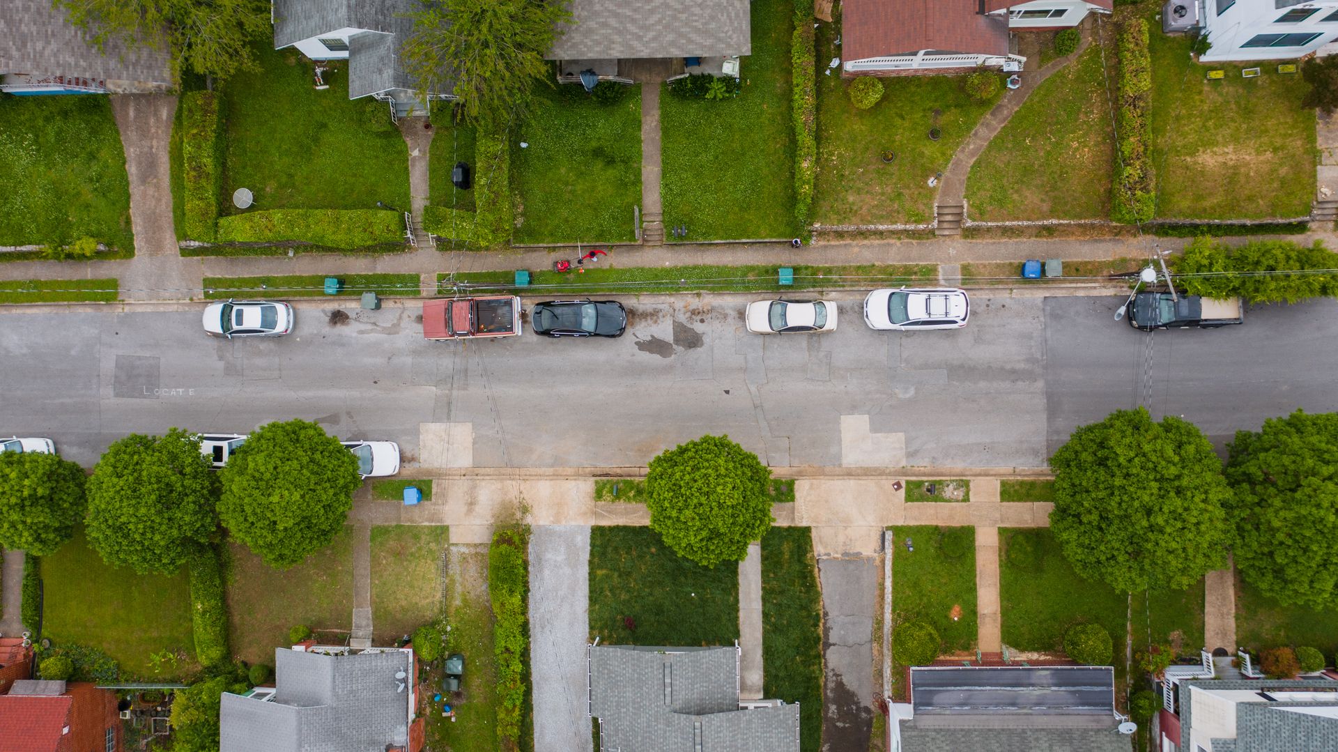Aerial view of a residential street with houses, lawns, and parked cars, showing building trust with neighbors